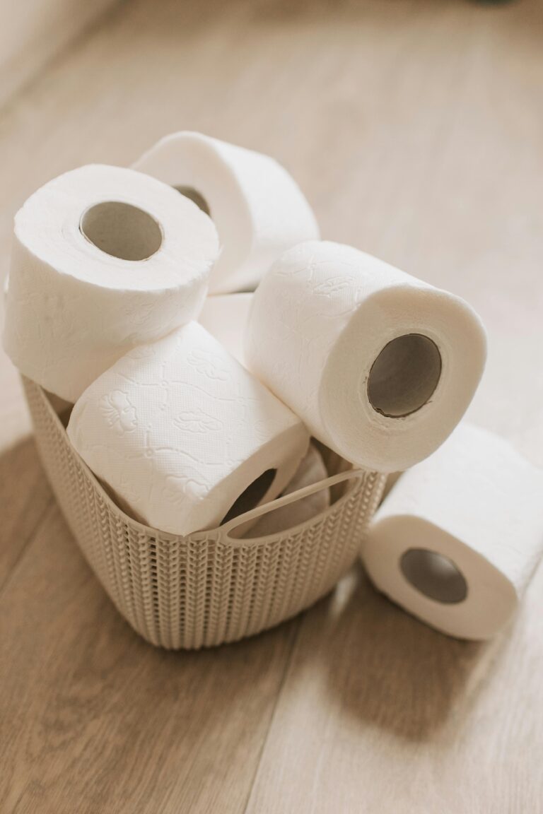 A wicker basket filled with toilet paper rolls sitting on a wooden floor, symbolizing hygiene essentials.